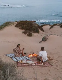 Two friends by a small campfire on the dunes above the sea.