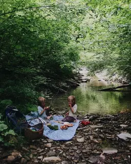 Two small children having a picnic beside a creek.